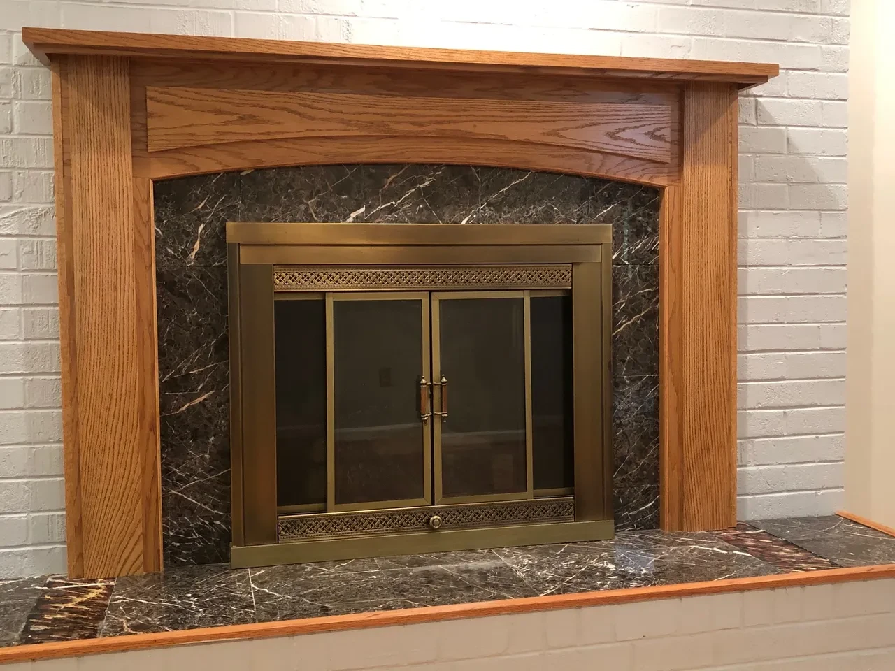Wooden fireplace with brass doors and marble surround